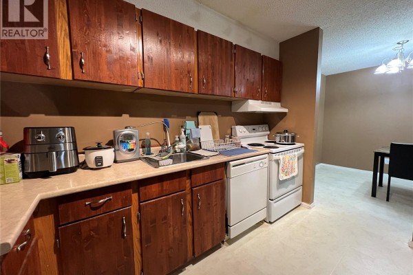 Kitchen with dark wood cabinets, beige countertops, white appliances, and a sink. - 410 510 Prairie Avenue, Saskatoon