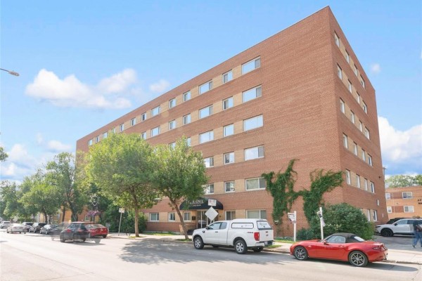 Exterior view of a five-story brick apartment building on a tree-lined street. - 410 565 Corydon Avenue, Winnipeg