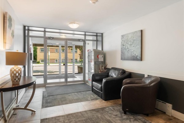 Building lobby with glass doors, two dark leather armchairs, a console table, and artwork. - 410 565 Corydon Avenue, Winnipeg