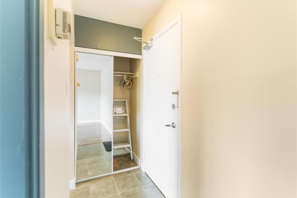 Hallway with a closet featuring mirrored sliding doors and a white apartment door. - 410 565 Corydon Avenue, Winnipeg
