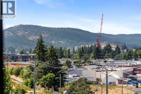 View from apartment window showing trees, buildings, and a distant red crane. - 410 777 Station Ave, Langford