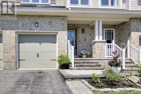 Close-up of a townhouse entrance with beige stone facade, single garage, and white railings. - 410 Ann Street, Mississippi Mills