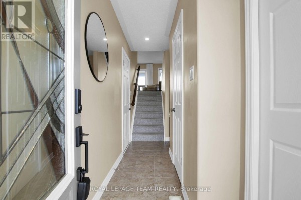 Hallway of a townhouse with tiled floor, beige walls, doors, and a staircase leading up. - 410 Ann Street, Mississippi Mills