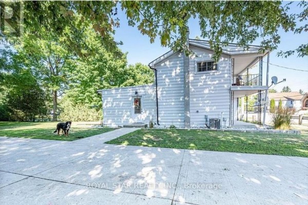 Rear exterior of a white house with a attached garage and green lawn, dog present. - 410 Main Street E, Norwich