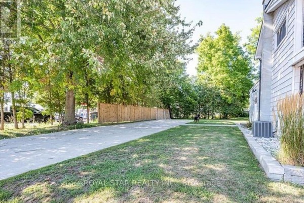 Long driveway leading to the rear of the property with grass and trees on the side. - 410 Main Street E, Norwich