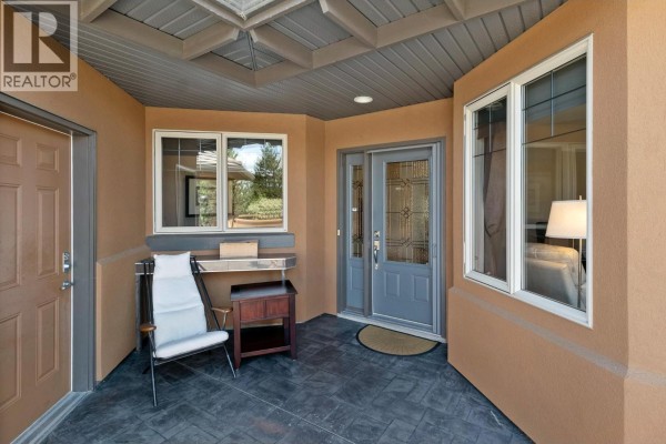 Covered entryway with a gray door, large windows, and a chair on the stamped concrete floor. - 4100 Gallaghers Parkland Drive Unit# 16, Kelowna