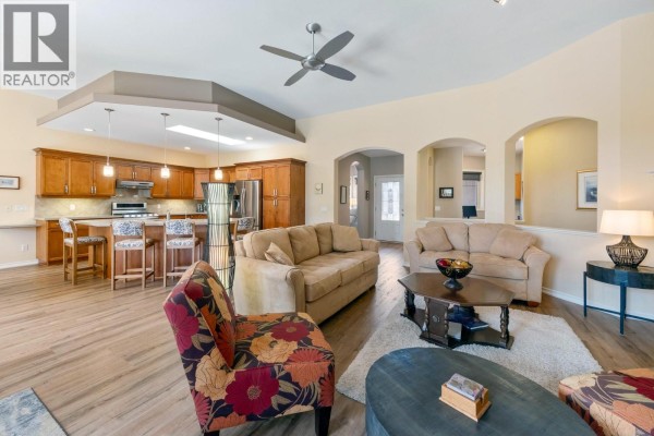 Living room with two sofas, a patterned armchair, coffee table, and open-concept kitchen view. - 4100 Gallaghers Parkland Drive Unit# 16, Kelowna