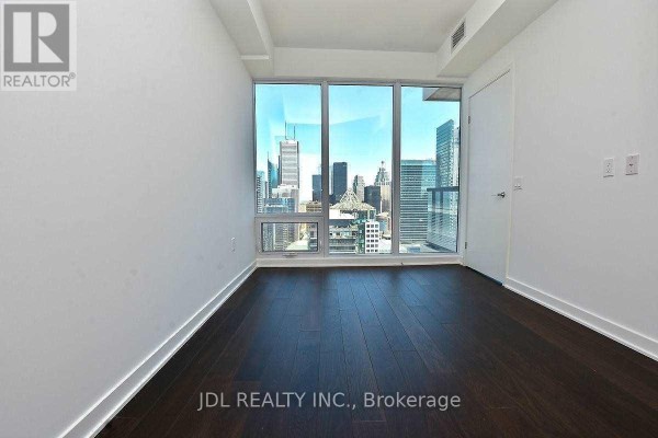 Empty room with dark wood floors and large windows showing city skyscrapers. - 4101 - 115 Blue Jays Way, Toronto