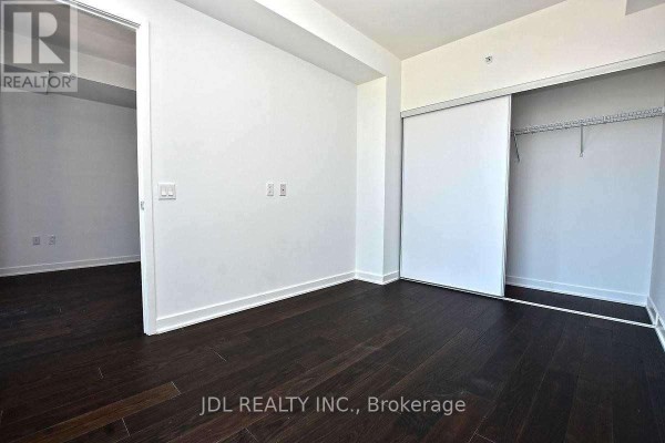 View of an empty room with dark wood floors connecting to another room. - 4101 - 115 Blue Jays Way, Toronto
