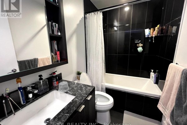 Bathroom with black tile, white bathtub, toilet, and dark vanity with sink. - 4101 - 115 Blue Jays Way, Toronto