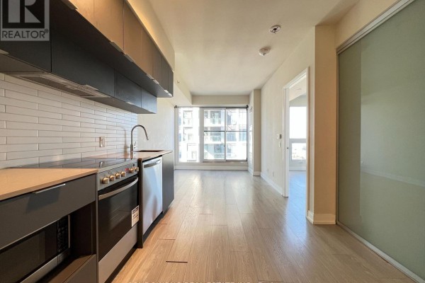 View of the living area from the kitchen, featuring light wood floors and large windows. - 4101 - 181 Dundas Street E, Toronto