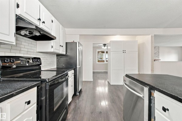 View of a kitchen with white cabinets, black granite countertops, stainless steel refrigerator, and stove. - 4102 48 Street, Bonnyville Town