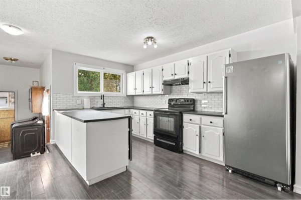Wide view of a kitchen featuring white cabinets, black countertops, and a stainless steel refrigerator. - 4102 48 Street, Bonnyville Town