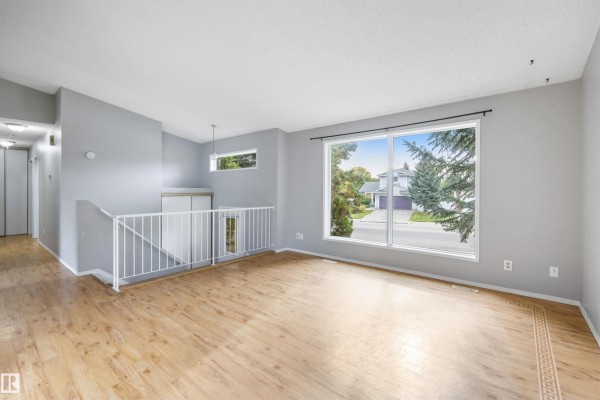 Living room with light wood floors, gray walls, a large window with a suburban view, and white railings. - 4105 44 Av, Stony Plain