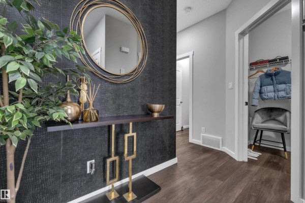 Hallway with a console table, round mirror, and open closet with clothing. - 4107 5 Av Sw, Edmonton