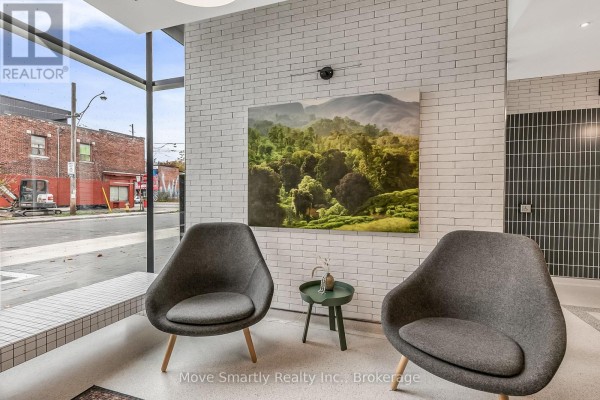 Lobby seating area with two grey armchairs, a side table, and a landscape painting. - 411 - 115 Larchmount Avenue, Toronto