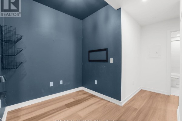 Corner room with dark blue walls, light wood floors, and a doorway to a bathroom. - 411 - 5 Wellington Street S, Kitchener