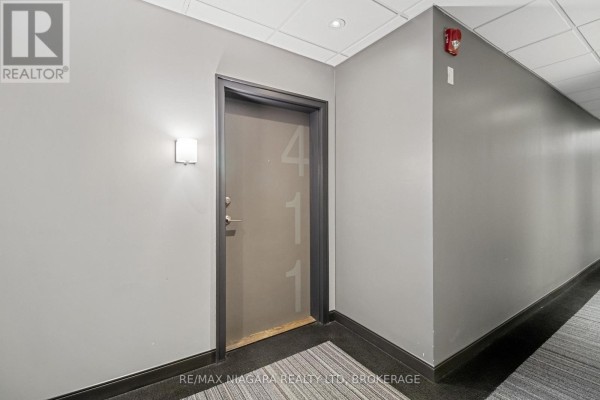 Hallway outside apartment 411 with gray walls, a light fixture, and a carpeted floor. - 411 - 520 North Service Road, Grimsby