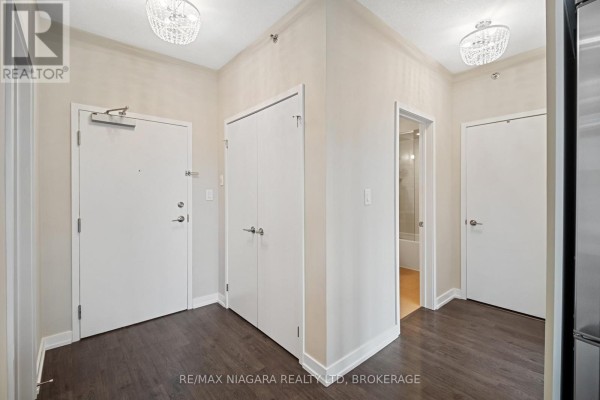 Apartment entryway with dark wood floors, two white doors, a closet, and two chandeliers. - 411 - 520 North Service Road, Grimsby