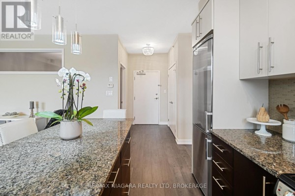 Kitchen with granite countertops, dark wood cabinets, stainless steel refrigerator, and pendant lights. - 411 - 520 North Service Road, Grimsby