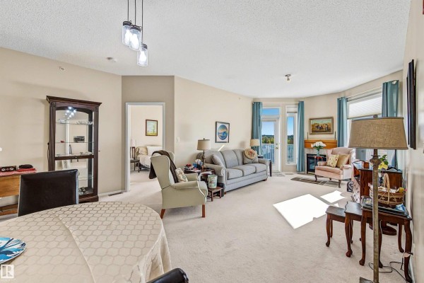 Living and dining area with beige carpet, fireplace, balcony door, and furniture. - #411 10 Ironwood Pt, St  Albert