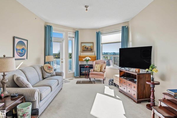 Living room featuring a grey sofa, fireplace, pink armchair, and television. - #411 10 Ironwood Pt, St  Albert