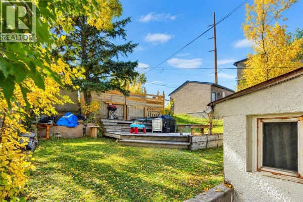 Backyard with a wooden deck, green grass, and trees with autumn leaves. - 411 33 Avenue Ne, Calgary