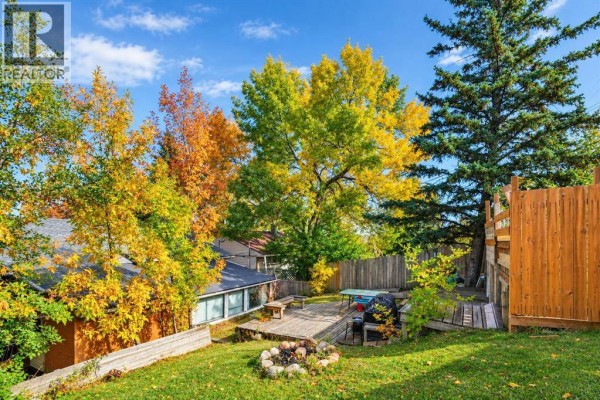 Backyard deck with a fire pit, grill, and fall foliage on trees. - 411 33 Avenue Ne, Calgary