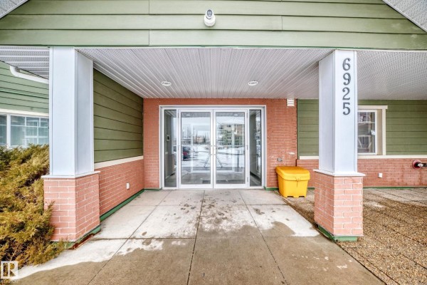 Apartment building lobby with mailboxes, seating, and glass doors leading outside. - #411 6925 199 St Nw Nw, Edmonton