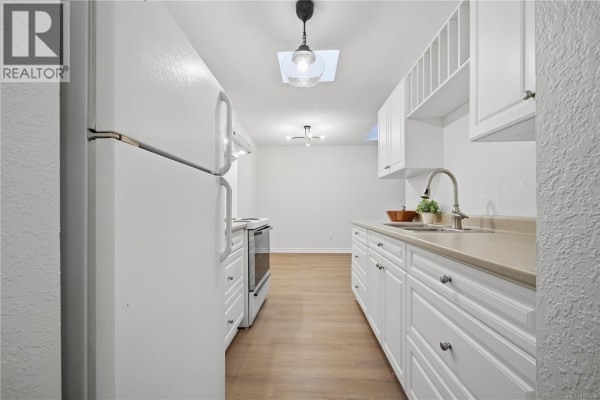 View down a white galley kitchen towards a dining area with light wood floors. - 411 909 Pembroke St, Victoria