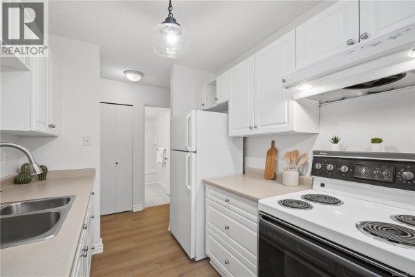 White galley kitchen with a refrigerator, stove, sink, and hallway entrance to a bathroom. - 411 909 Pembroke St, Victoria
