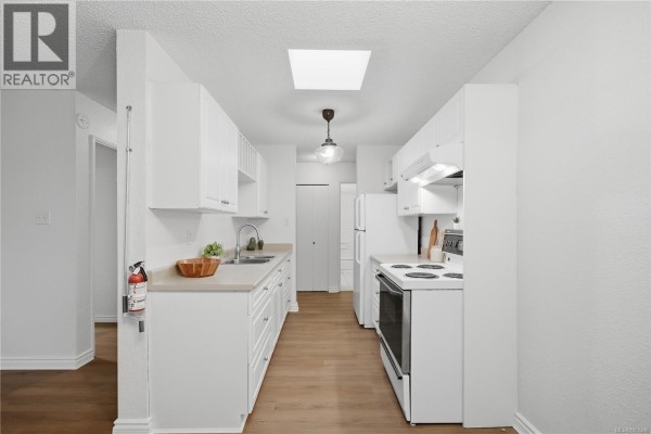 White galley kitchen with a skylight, light wood floors, beige countertops, and white cabinets. - 411 909 Pembroke St, Victoria