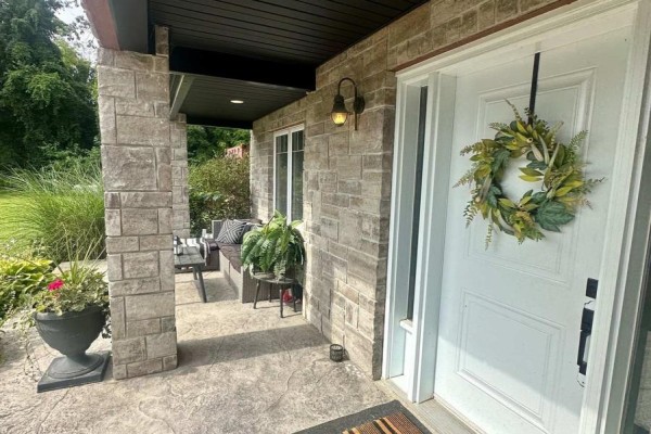 Covered front porch with stone columns, a white door, and outdoor seating. - 41108 Sparta Line, Southwold