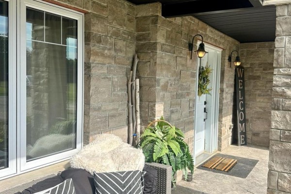 Close-up of a front porch with stone siding, a white door, and a welcome sign. - 41108 Sparta Line, Southwold