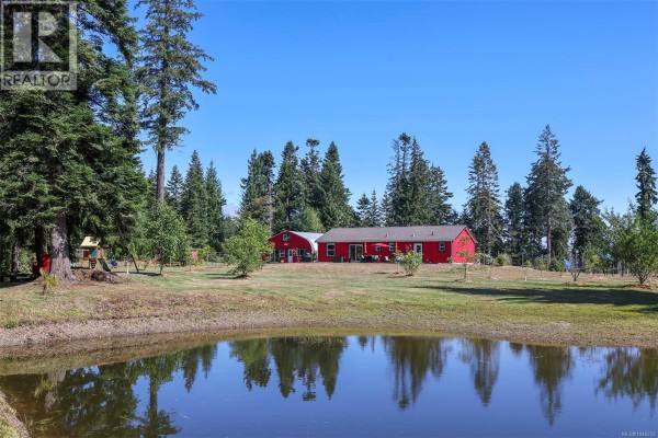 Red house and Quonset hut with a pond in the foreground reflecting trees and sky. - 4114 Island Hwy S, Campbell River