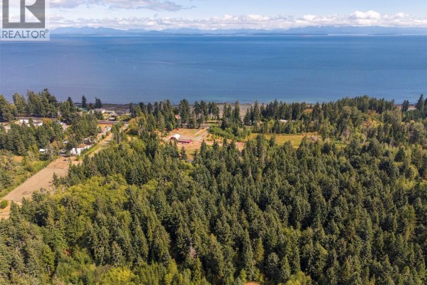 Aerial view of the coastal property with a red house, forest, and ocean in the background. - 4114 Island Hwy S, Campbell River