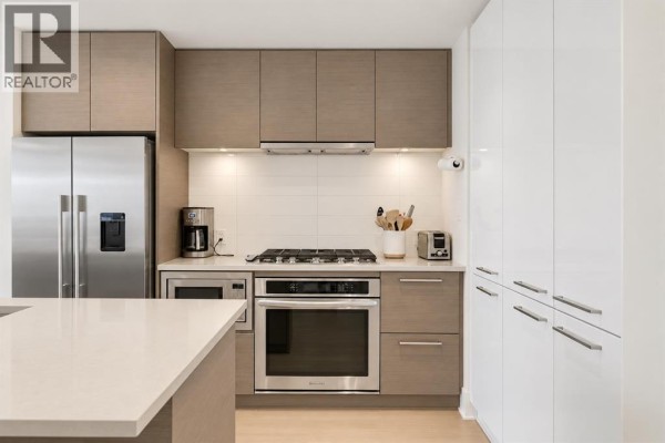 Modern kitchen with dark wood cabinets, island, stainless steel appliances, and open living area. - 412, 38 9 Street Ne, Calgary