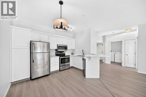 Kitchen with white cabinets, stainless steel appliances, light grey flooring, and view to hallway. - 412, 777 3 Avenue Sw, Calgary