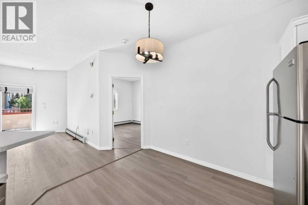 Living area with white walls, fireplace, and view through sliding glass doors to balcony. - 412, 777 3 Avenue Sw, Calgary