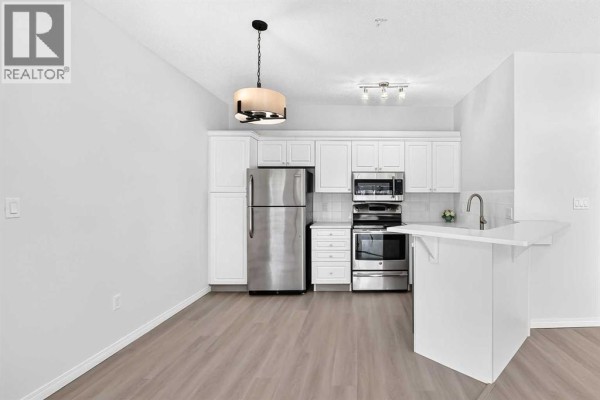 Kitchen with white cabinetry, stainless steel appliances, and breakfast bar overlooking living space. - 412, 777 3 Avenue Sw, Calgary