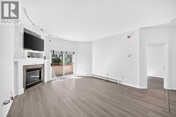 Living room with fireplace, entertainment unit, sliding glass doors, and view into hallway. - 412, 777 3 Avenue Sw, Calgary