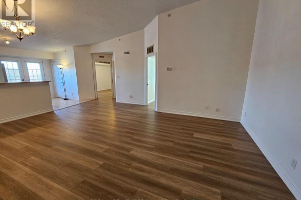 Living area with wood-look laminate flooring, doorway to kitchen, and access to balcony. - 412 - 4025 Kilmer Drive, Burlington