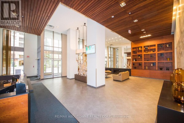 Lobby with wood ceilings, glass doors, a stone fireplace, and a reception desk. - 412 - 4080 Living Arts Drive, Mississauga