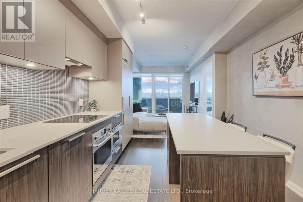Kitchen island with three stools, grey backsplash, and view into hallway and bedroom. - 412 - 4208 Dundas Street W, Toronto