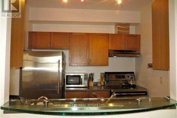 Compact kitchen with stainless steel appliances, wood cabinets, and a glass counter. - 412 - 438 Richmond Street W, Toronto
