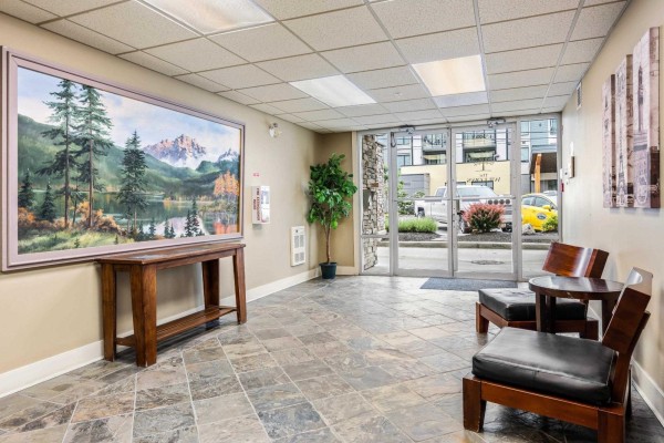 Apartment building lobby with tile floor, wood console table, chairs, and large landscape painting. - 412 45893 Chesterfield Avenue, Chilliwack Downtown, Chilliwack