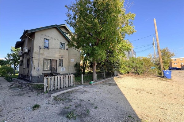 Rear exterior of the commercial building with a gravel parking area and a wooden fence. - 412 Wardlaw Avenue, Winnipeg