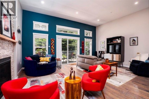 Living room with a teal accent wall, fireplace, large windows, and comfortable seating. - 4128 Emerald Woods Pl, Nanaimo