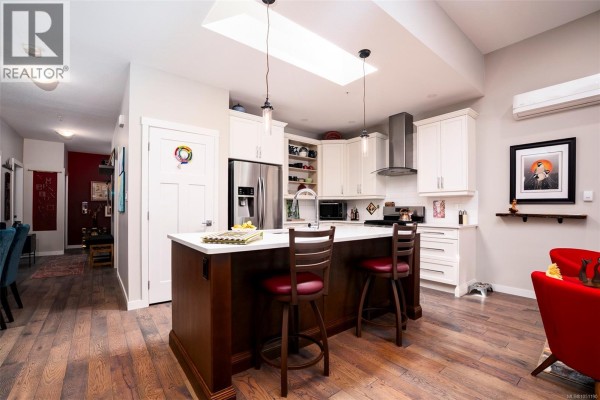 Modern kitchen with white cabinets, a large island with bar stools, and stainless steel appliances. - 4128 Emerald Woods Pl, Nanaimo