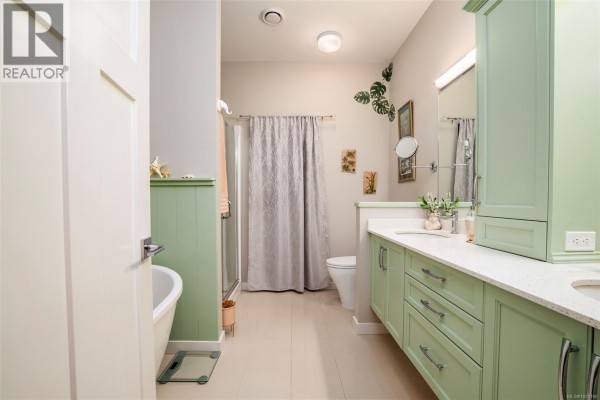Spacious bathroom with green double vanity, bathtub, glass shower, and tile flooring. - 4128 Emerald Woods Pl, Nanaimo